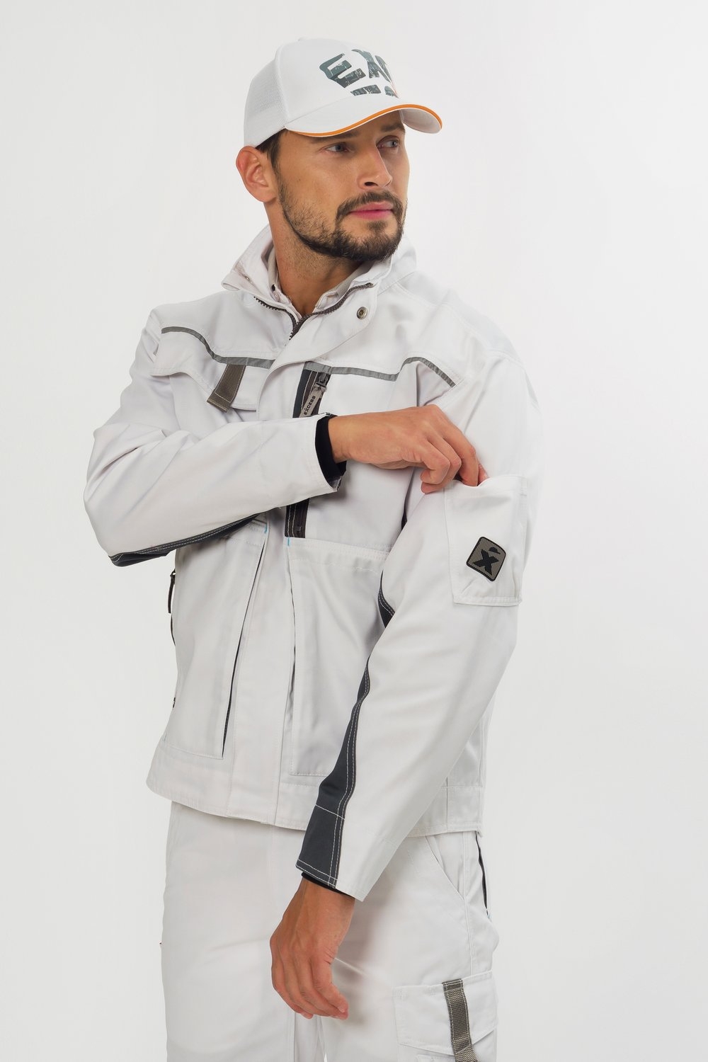 Weiße Arbeitsjacke mit Reißverschluss – moderne Arbeitskleidung von EXCESS, getragen von Mann mit weißer Hose und passender Cap.