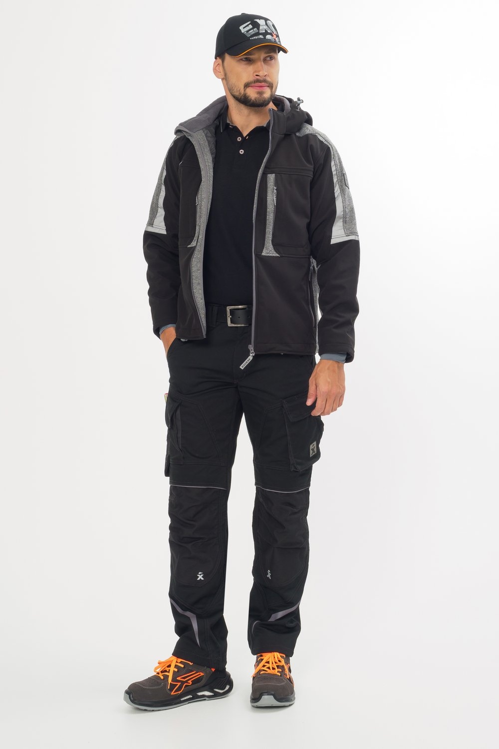 Mann trägt schwarze Arbeitsjacke mit grauen Details, schwarze Arbeitshose mit Taschen, Cap und Sicherheitsschuhe.