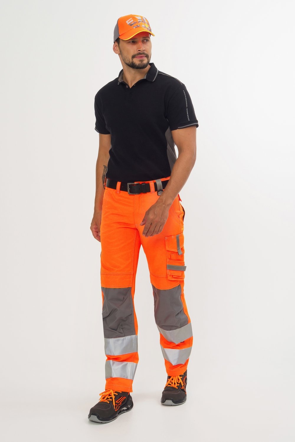 Mann trägt schwarzes Poloshirt, orangefarbene Warnschutzhose mit grauen Knieeinsätzen und Reflexstreifen sowie schwarze Sicherheitsschuhe.
