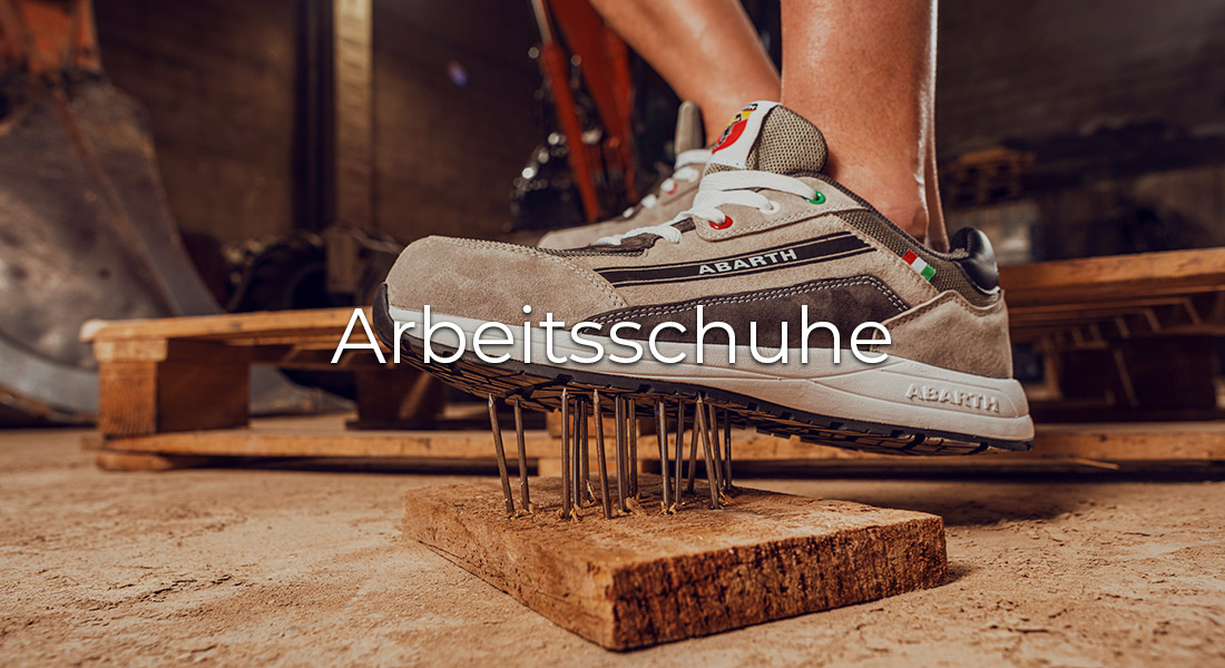 Grauer Abarth-Arbeitsschuh steht auf einem Brett mit herausragenden Nägeln, um seine Durchtrittsicherheit zu demonstrieren. Text „Arbeitsschuhe“ steht mittig über dem Bild.