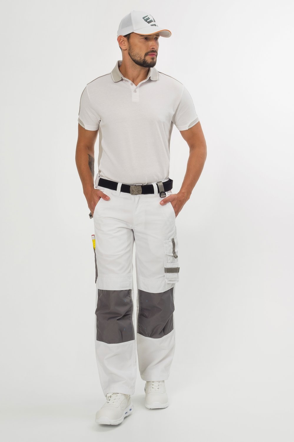Ein Mann trägt helles Poloshirt, weiße Arbeitshose mit grauen Knieverstärkungen, schwarzen Gürtel, weiße Cap und weiße Schuhe.