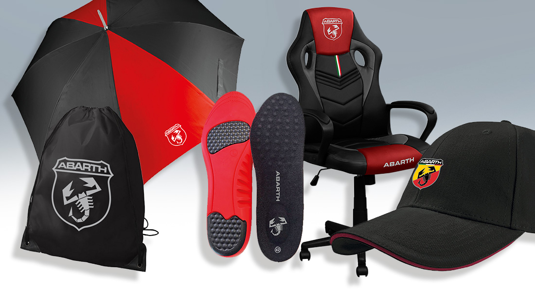 Abarth-Merchandising-Produkte auf hellem Hintergrund: schwarzer und roter Regenschirm, schwarzer Turnbeutel mit Logo, rote und schwarze Schuhsohlen, ergonomischer Gaming-Stuhl mit Abarth-Emblem und schwarze Kappe mit gelb-rotem Logo.