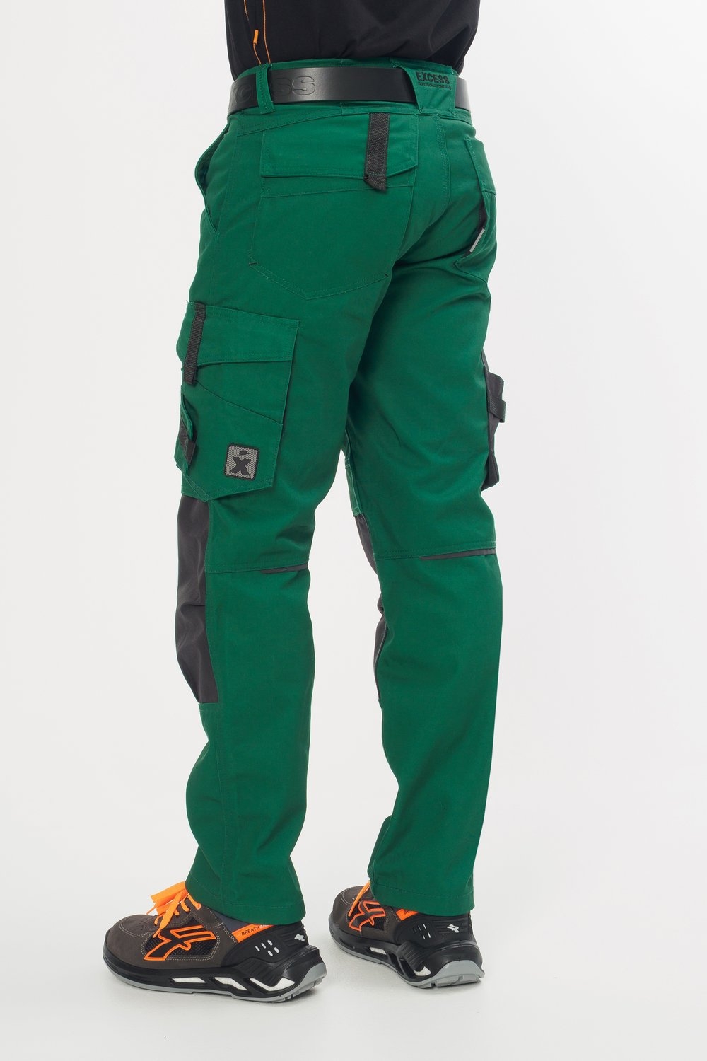 Rückansicht einer grünen Arbeitshose mit schwarzen Knieverstärkungen, seitlichen Cargotaschen und Gesäßtaschen. Getragen von einem Handwerker mit schwarzem Gürtel und Arbeitsschuhen mit orangefarbenen Akzenten.
