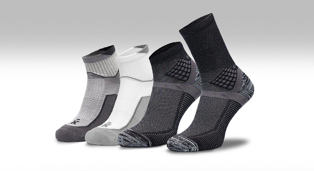 Vier Paar Arbeitssocken in unterschiedlichen Grautönen von hell bis dunkel stehen nebeneinander vor neutralem Hintergrund.