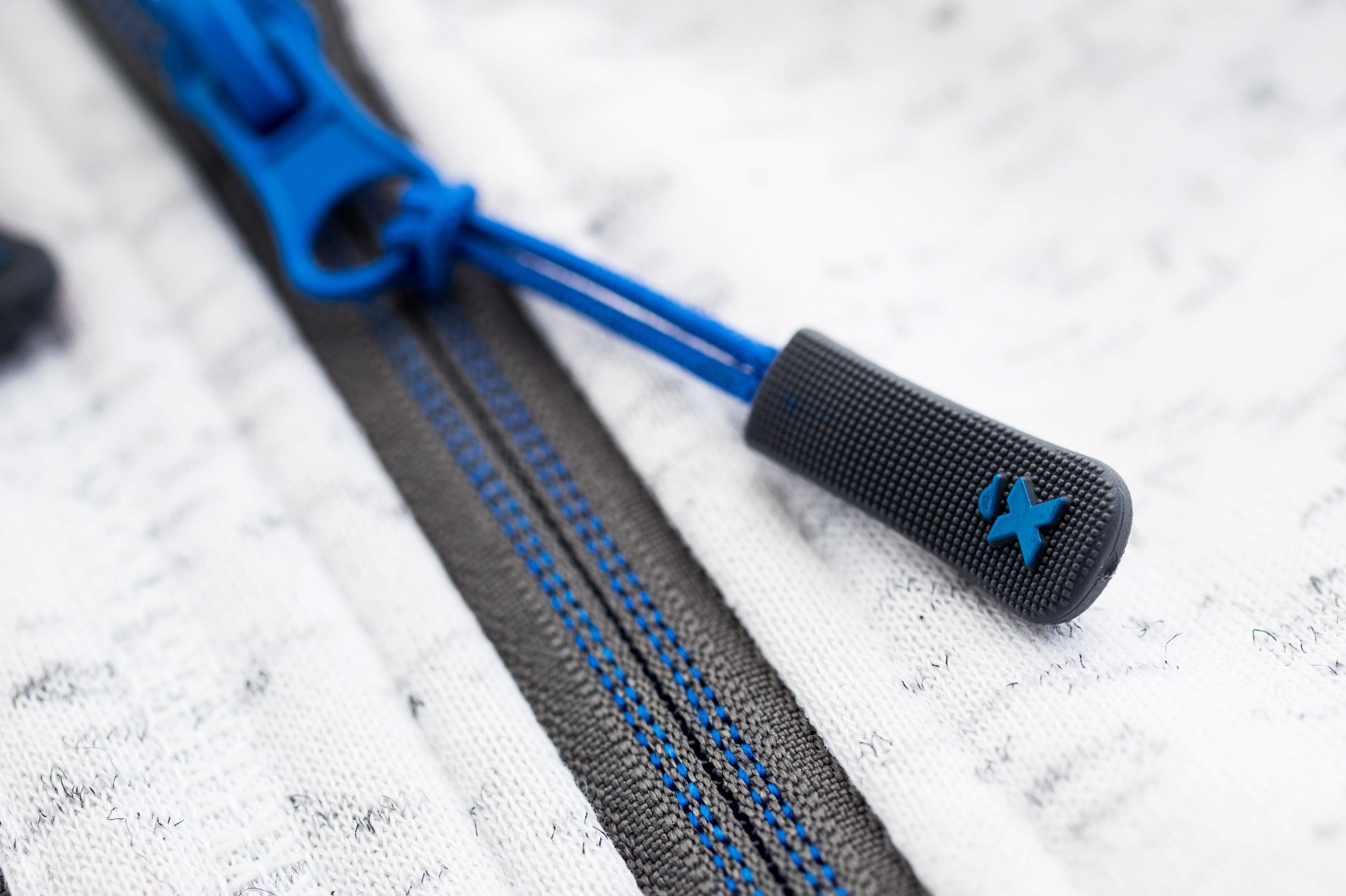 Excess Workwear Jacke Detail, Nahaufnahme blauer Reißverschluss mit schwarzem Zippergriff und geprägtem X-Logo.