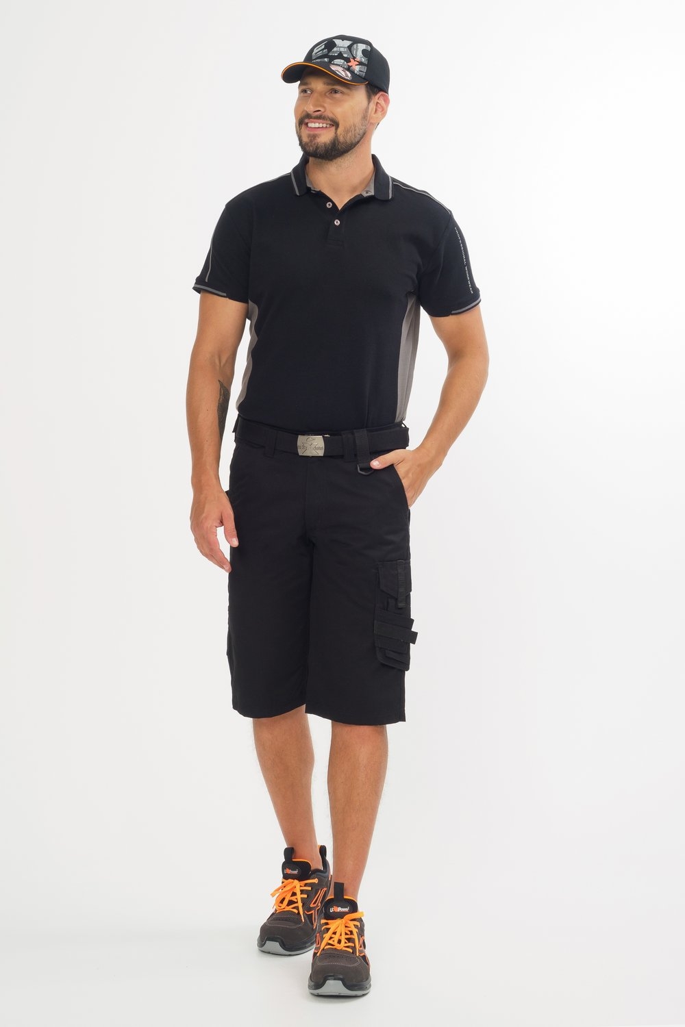 Mann trägt schwarzes Poloshirt, schwarze Arbeitsshorts mit Taschen, schwarze Cap und Arbeitsschuhe mit orangefarbenen Details.