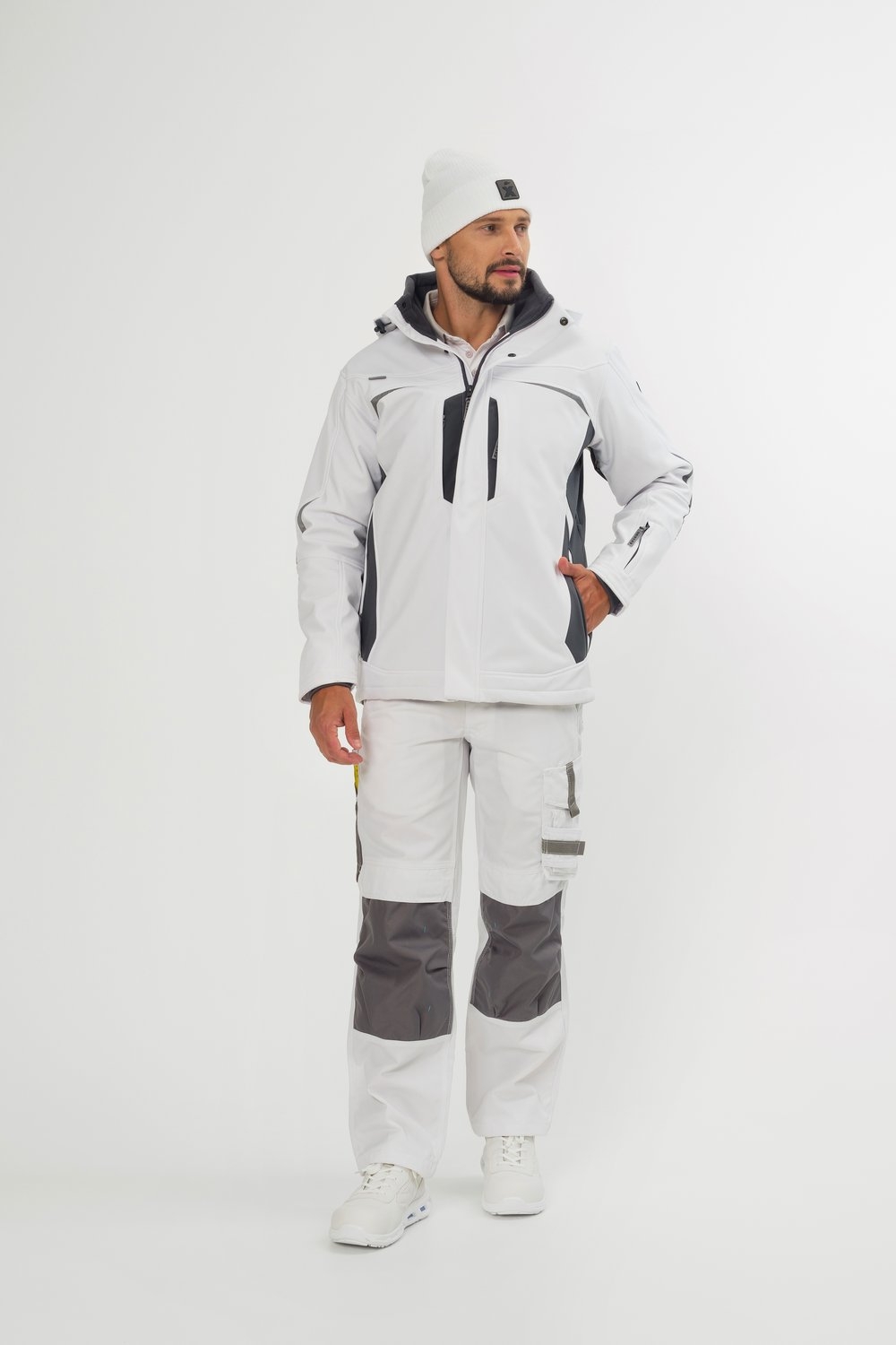 Weiße Softshelljacke von Excess Workwear, getragen von einem Modell. Die Jacke hat graue Einsätze, eine Kapuze, ein Logo am unteren Rücken sowie ergonomischen Schnitt. Kombiniert mit passender Arbeitshose, Arbeitsschuhen und Mütze.