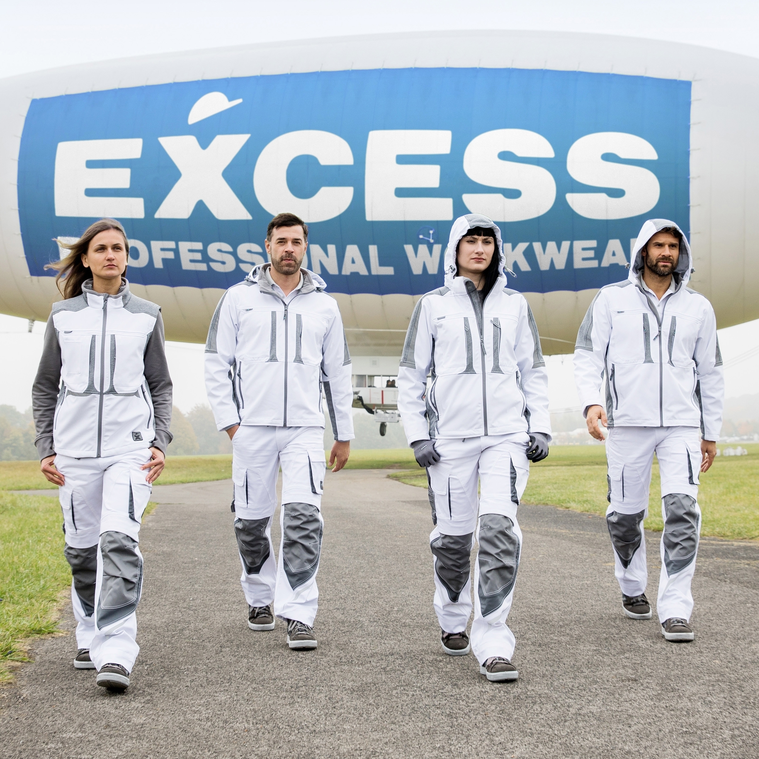 EXCESS Workwear – moderne weiße Arbeitskleidung mit grauen Details, präsentiert von vier Personen vor großem Luftschiff.