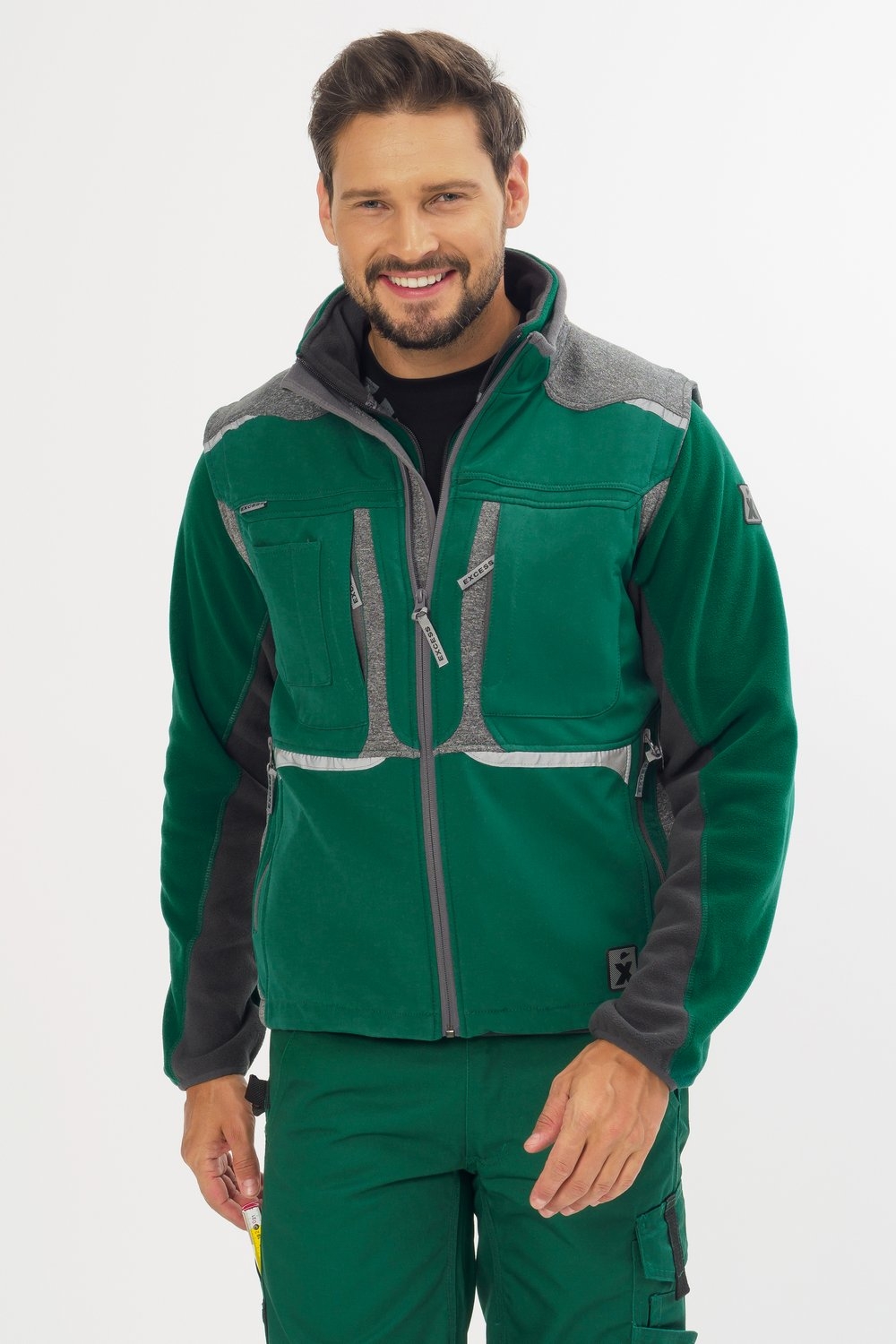 Ein Mann in grüner Fleecejacke mit grauen Schulter- und Brustdetails, mehreren Reißverschlusstaschen und passender Arbeitshose.