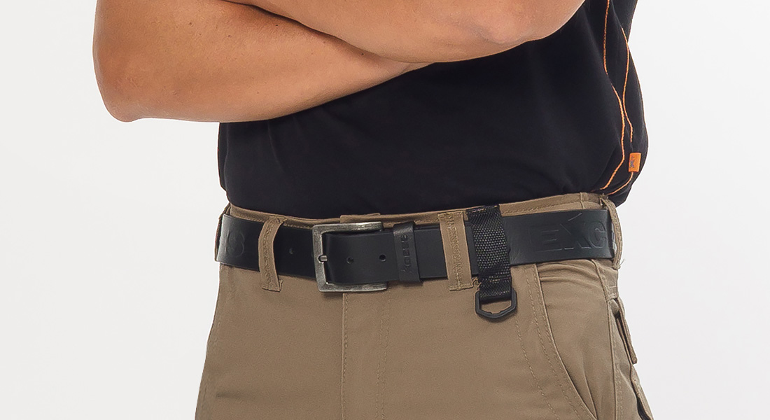 Ausschnitt einer Person mit verschränkten Armen, die eine schwarze Arbeitsgürtelschnalle und beigefarbene Arbeitshose trägt.
