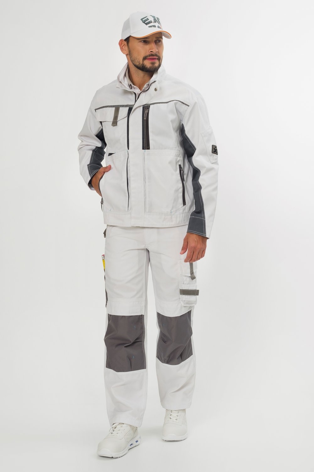 Weiße Arbeitsjacke mit Reißverschluss – moderne Arbeitskleidung von EXCESS, getragen von Mann mit weißer Hose und passender Cap.