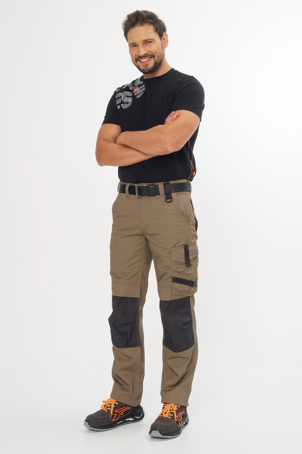 Braune Arbeitshose mit schwarzen Knieverstärkungen und Taschen – robuste Workwear kombiniert mit schwarzem T-Shirt und Sicherheitsschuhen.